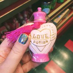 a hand holding a small bottle with a pink tassel on it and the words love potion written on it