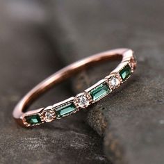 an emerald and diamond band ring sitting on top of a rock