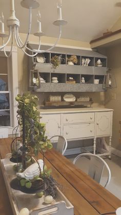 a wooden table topped with lots of white plates and vases next to a shelf filled with dishes