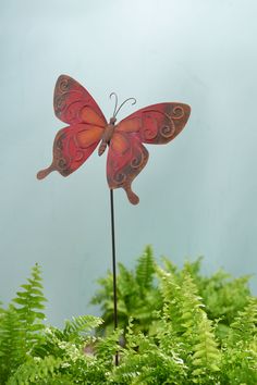 a red butterfly statue sitting on top of a green plant