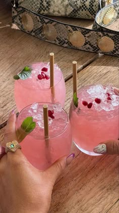 three pink cocktails with garnish on the rim and one being held by a woman's hand