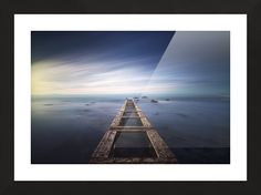 a long pier extending into the ocean under a cloudy sky with rocks in the water