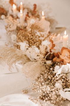 flowers and candles are lined up on a white tablecloth with gold trimmings