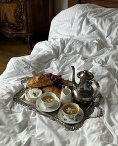 a tray filled with food sitting on top of a bed next to a silver tea pot