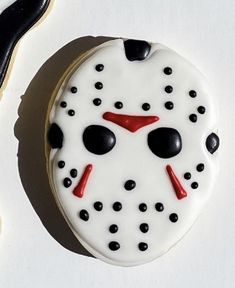 a cookie decorated to look like a mask with black dots and red eyes is next to a pair of scissors