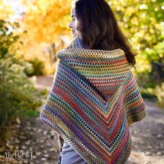 a woman wearing a multicolored crocheted shawl in the fall leaves