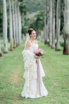 a woman in a white dress holding a bouquet and standing next to some palm trees