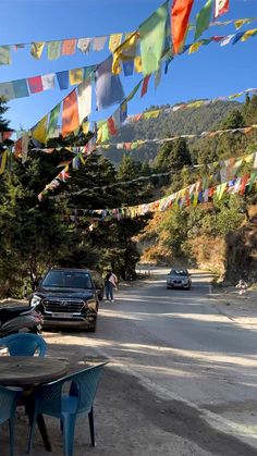 cars parked on the side of a road with colorful flags hanging above it and people walking down the street