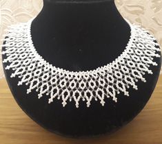 a white beaded necklace on a black display stand