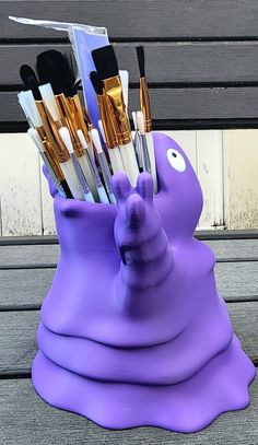 a purple vase with brushes in it sitting on a bench