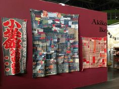 quilts on display at an art fair with banners hanging from the wall behind them