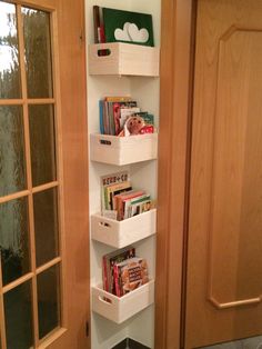 a white shelf with books and magazines on it in front of a wooden door next to a window