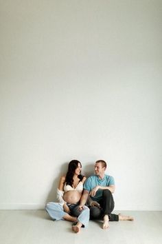 a man and woman sitting on the floor next to each other in front of a white wall