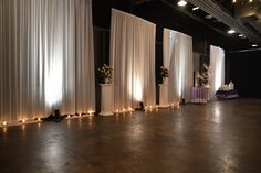 an empty room with white drapes and candles on the floor, decorated with flowers