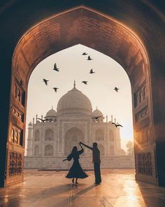 two people standing in front of a building with birds flying around