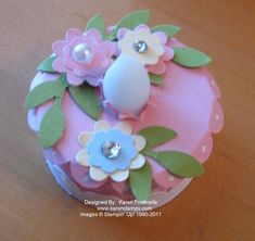 a pink cupcake with flowers and pearls on it's top sitting on a table