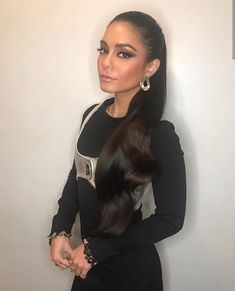 a woman with long hair standing in front of a white wall wearing a black dress