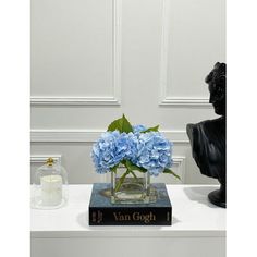 a vase filled with blue flowers sitting on top of a book next to a statue