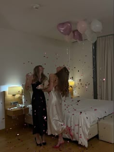 two women standing on a bed with balloons and confetti