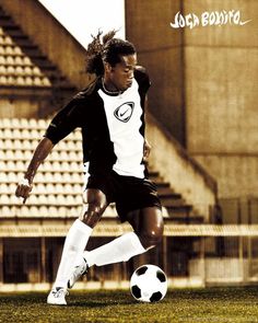 a young man kicking a soccer ball on top of a field with bleachers in the background