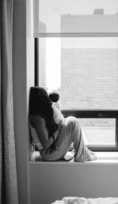 a woman is sitting on a window sill with her head in her hands and looking out the window