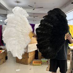 a man in black shirt standing next to large white feathers