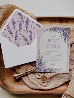 the wedding stationery is laid out on a wooden tray with an envelope and key