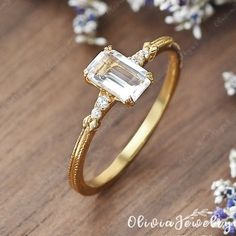 a gold ring with an emerald stone in the center on a wooden surface surrounded by flowers