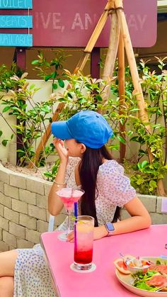 a woman sitting at a pink table with a blue hat on her head and a drink in front of her