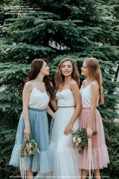 three young women standing next to each other in front of some trees and greenery