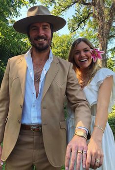 a man and woman dressed in wedding attire standing next to each other with their hands together