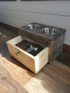 a wooden box with two bowls and spoons in it sitting on the floor next to a dog bowl