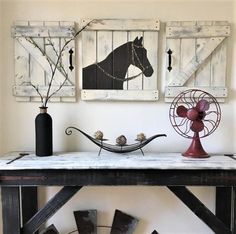 a wooden table topped with art pieces next to a fan and vase filled with flowers