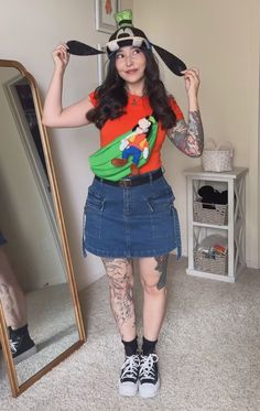 a woman with tattoos is standing in front of a mirror wearing a mickey mouse t - shirt