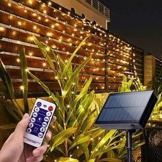 a hand holding a remote control in front of a solar panel with lights on it