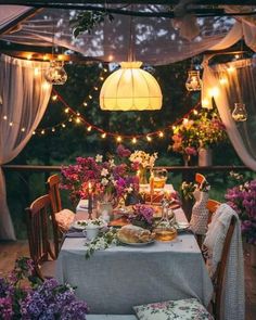 an outdoor dining area with flowers and lights strung over the table, surrounded by curtains