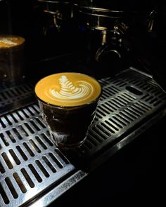 a cup of coffee sitting on top of a metal grate next to another cup