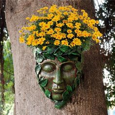 a green man's face with yellow flowers growing out of it on the side of a tree