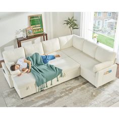 a woman laying on top of a white couch in a living room next to a window