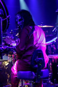 a man sitting on top of a chair in front of a drum set with purple lighting behind him