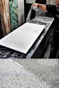 a man is spraying water on a marble counter top in front of a large painting