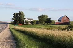 an empty country road in the middle of a field with houses and trees on either side