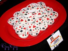 a red plate topped with cupcakes covered in white frosting and playing cards