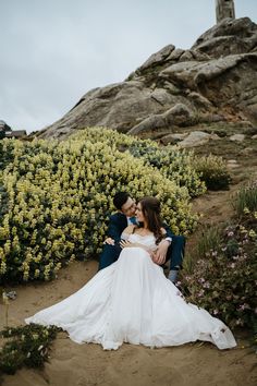 a bride and groom sitting on the sand in front of flowers