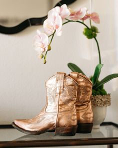 a pair of cowboy boots sitting on top of a table next to a vase with flowers