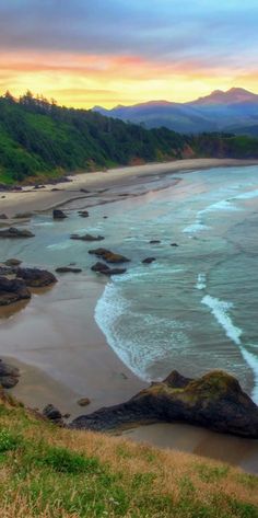 the beach is surrounded by green hills and trees, with waves coming in from the ocean