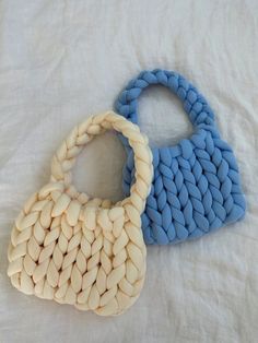 two bags made out of woven material sitting on a white bed sheet, one is blue and the other is beige