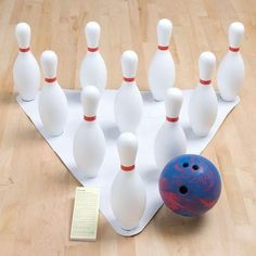 a group of white bowling pins and a blue ball on a wooden floor with a note