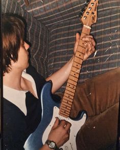 a man sitting on a couch with a guitar in his hand and looking at it