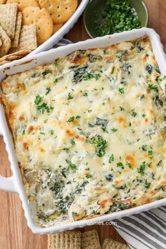 spinach and cheese dip in a white casserole dish with crackers on the side